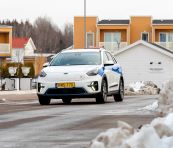 En vit elbil strajpad i Länstrafikens färger kör i ett bostadsområde med snövallar.  
