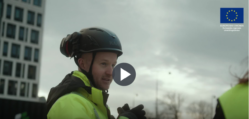 En man i varselkläder på ett bygge, en playikon för att starta filmen