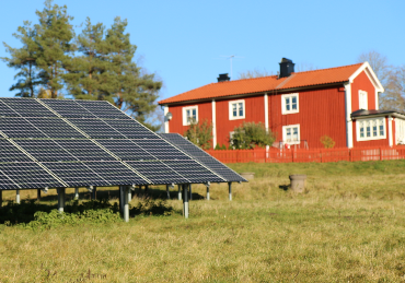 Solceller i en hage. I bakgrunden ett rött hus.